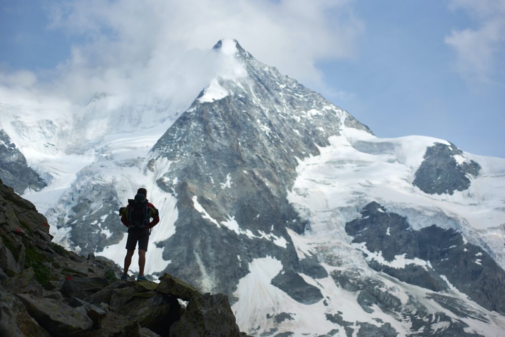 Male tourist climbing snowy rocky cliffs of beautiful Penning Alps in Switzerland